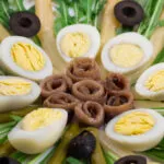 Uova sode tagliate a metà in un'insalata con acciughe e olive