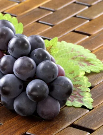Grappolo di uva nera con la pruina bianca ben visibile sugli acini, appoggiato su un piano di legno