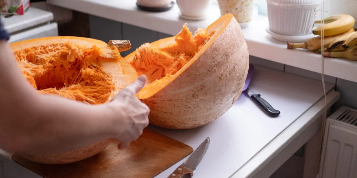 Grande zucca appena tagliata in due metà su un piano di cucina, con la polpa arancione filamentosa in vista e due coltelli appoggiati accanto