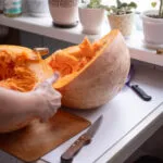 Grande zucca appena tagliata in due metà su un piano di cucina, con la polpa arancione filamentosa in vista e due coltelli appoggiati accanto