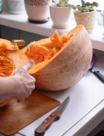 Grande zucca appena tagliata in due metà su un piano di cucina, con la polpa arancione filamentosa in vista e due coltelli appoggiati accanto