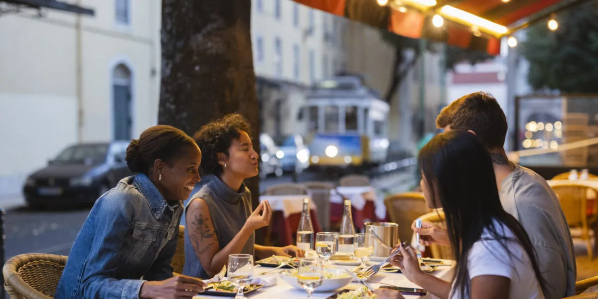 Amici che cenano sorridenti nel dehors di un ristorante con luci calde serali