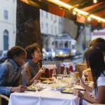 Amici che cenano sorridenti nel dehors di un ristorante con luci calde serali