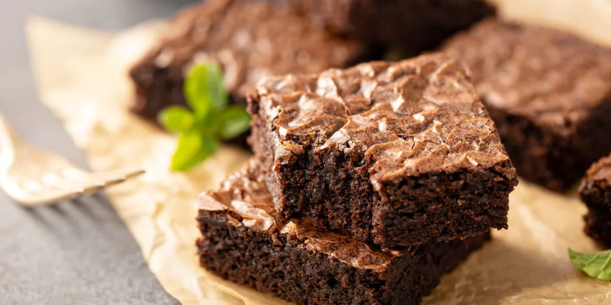 Quadrotti di brownie al cioccolato con la superficie lucida e screpolata su carta da forno