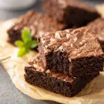 Quadrotti di brownie al cioccolato con la superficie lucida e screpolata su carta da forno