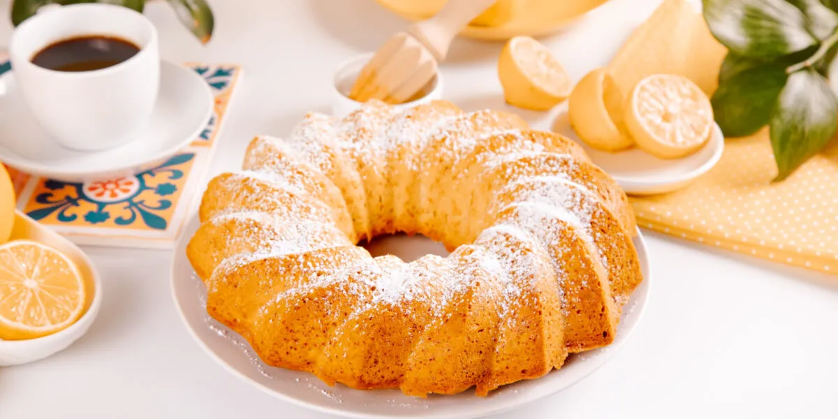 Ciambella intera spolverizzata di zucchero a velo con caffè e limoni sul tavolo della colazione
