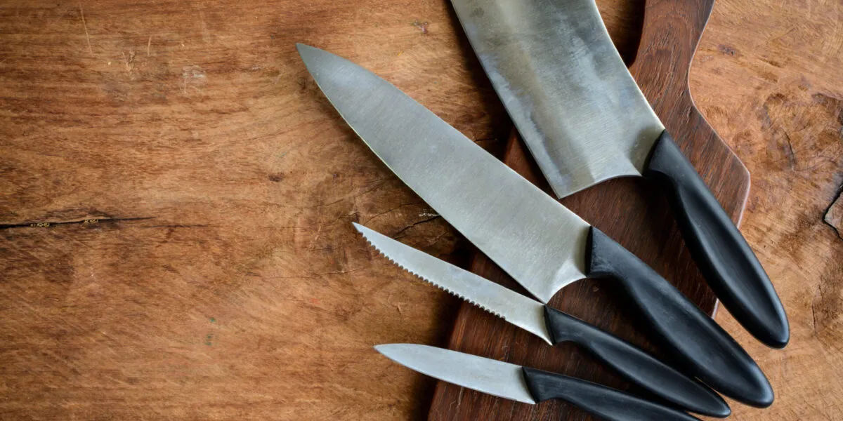 Coltello da chef, coltello seghettato, spelucchino e mannaia appoggiati su un tagliere di legno scuro