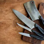 Coltello da chef, coltello seghettato, spelucchino e mannaia appoggiati su un tagliere di legno scuro