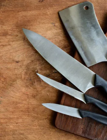Coltello da chef, coltello seghettato, spelucchino e mannaia appoggiati su un tagliere di legno scuro