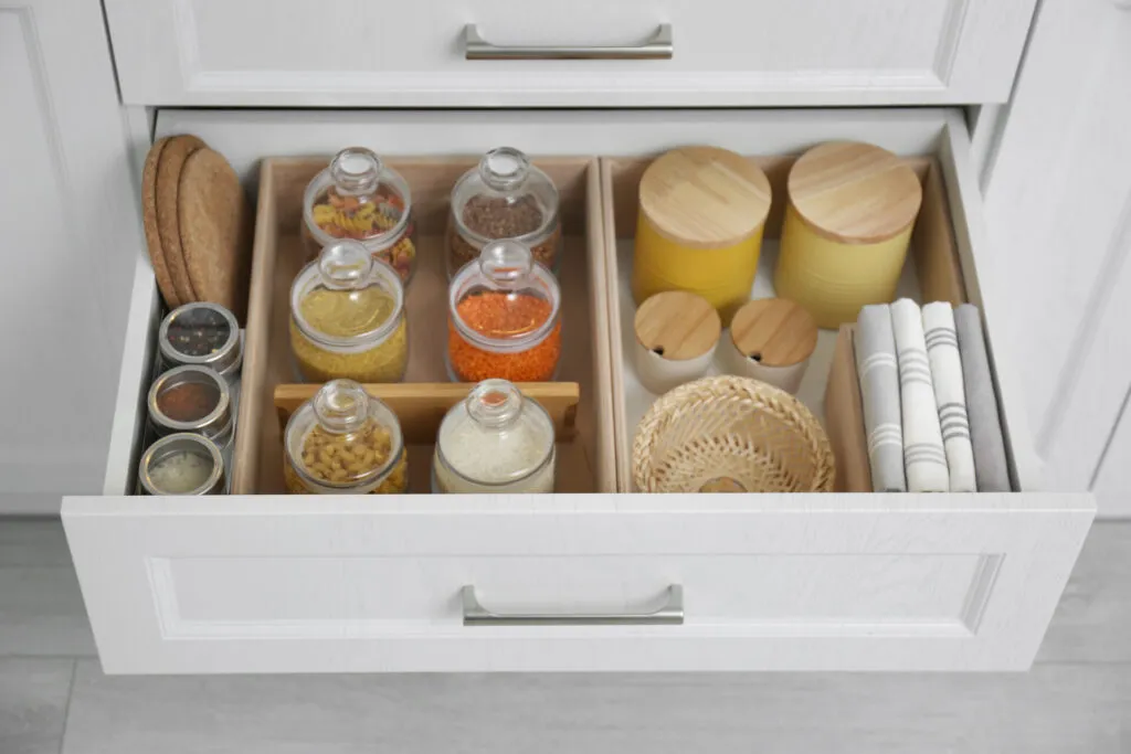 Cassetto da cucina aperto e organizzato con barattoli chiusi di spezie, pasta, riso e legumi e contenitori con coperchio in legno