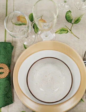 Tavola apparecchiata per una persona con tovaglia a limoni, piatti in ceramica e tovagliolo verde