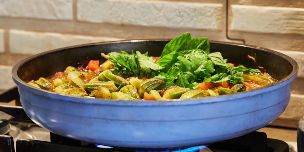 Padella troppo piena di verdure e pomodoro che cuociono nel loro liquido sul fornello acceso