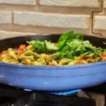 Padella troppo piena di verdure e pomodoro che cuociono nel loro liquido sul fornello acceso