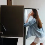 Donna davanti al frigorifero aperto con un dito sulle labbra, indecisa su cosa mangiare