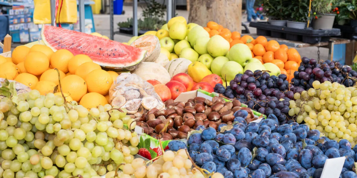 Banco di frutta autunnale al mercato con uva, prugne, castagne, mele e mandarini