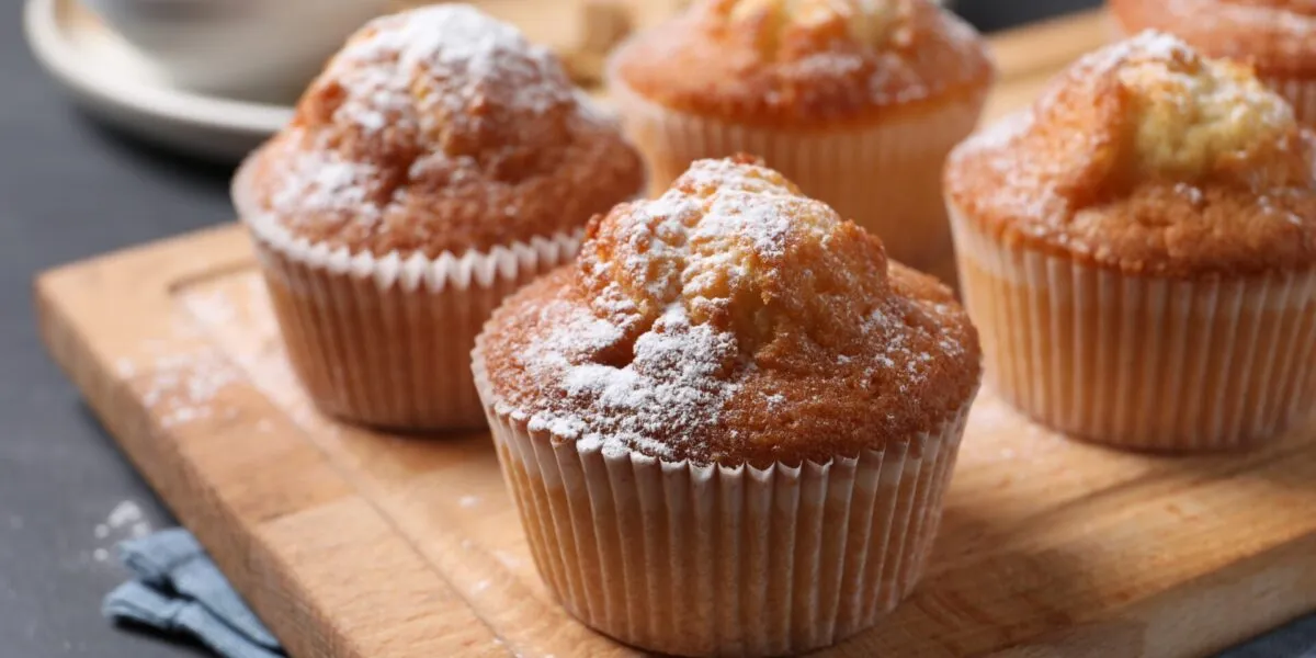 Muffin con la cupola dorata spolverizzati di zucchero a velo su un tagliere di legno