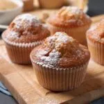 Muffin con la cupola dorata spolverizzati di zucchero a velo su un tagliere di legno