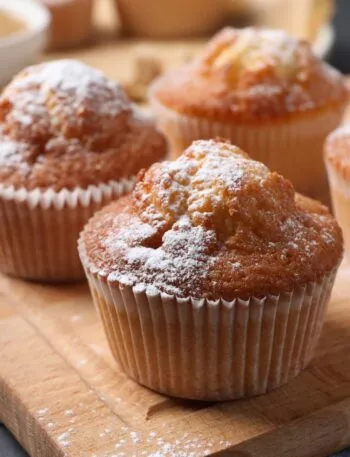 Muffin con la cupola dorata spolverizzati di zucchero a velo su un tagliere di legno