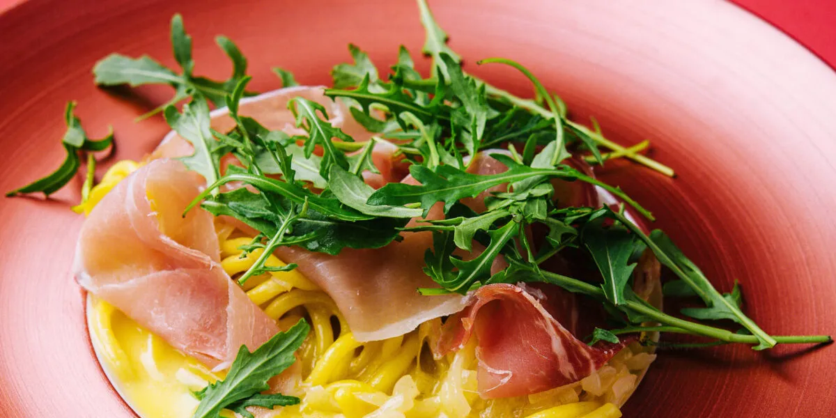 Spaghetti con salsa cremosa, prosciutto crudo e rucola fresca in un piatto rosso