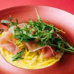 Spaghetti con salsa cremosa, prosciutto crudo e rucola fresca in un piatto rosso