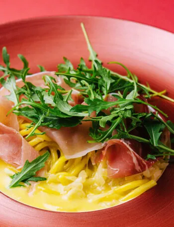 Spaghetti con salsa cremosa, prosciutto crudo e rucola fresca in un piatto rosso