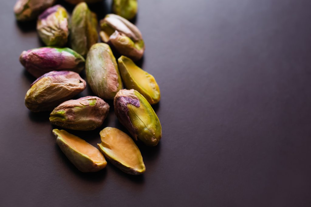 Pistacchi sgusciati con pellicina violacea e semi spaccati a metà su fondo scuro