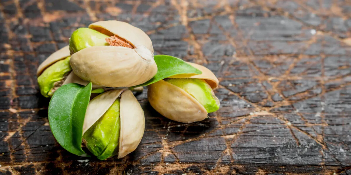 Pistacchi con il guscio socchiuso e il seme verde in vista su un tagliere di legno scuro