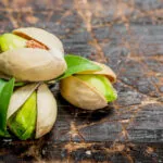 Pistacchi con il guscio socchiuso e il seme verde in vista su un tagliere di legno scuro