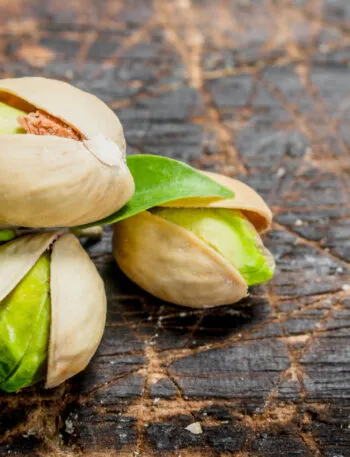 Pistacchi con il guscio socchiuso e il seme verde in vista su un tagliere di legno scuro