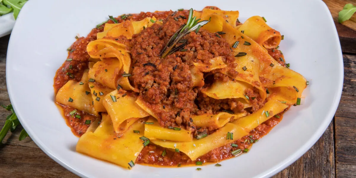 Piatto di pappardelle al ragù con rosmarino fresco su un tavolo di legno