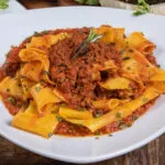 Piatto di pappardelle al ragù con rosmarino fresco su un tavolo di legno