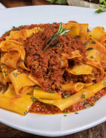 Piatto di pappardelle al ragù con rosmarino fresco su un tavolo di legno