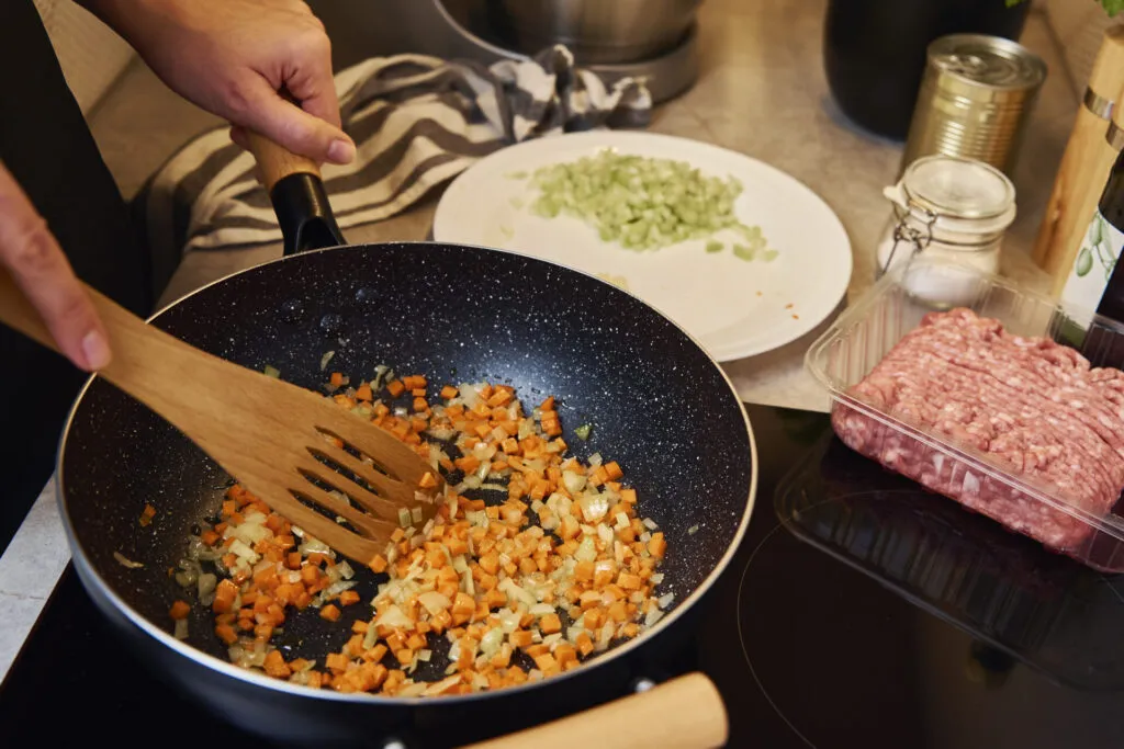 Cipolla e carota tritate che appassiscono in padella, con sedano tritato e macinato pronti accanto