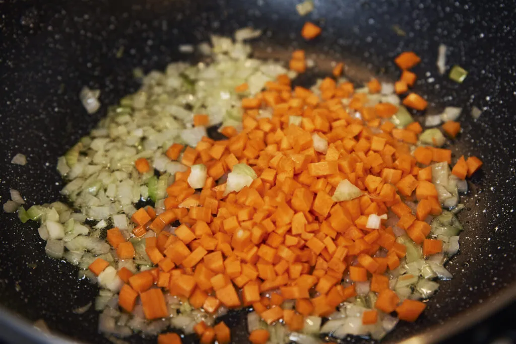 Cipolla, carota e sedano tritati finemente che soffriggono in una padella antiaderente con un filo d’olio