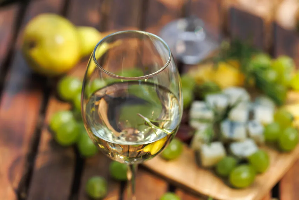 Calice di vino bianco su un tavolo di legno all’aperto, con grappoli d’uva bianca e pere sullo sfondo
